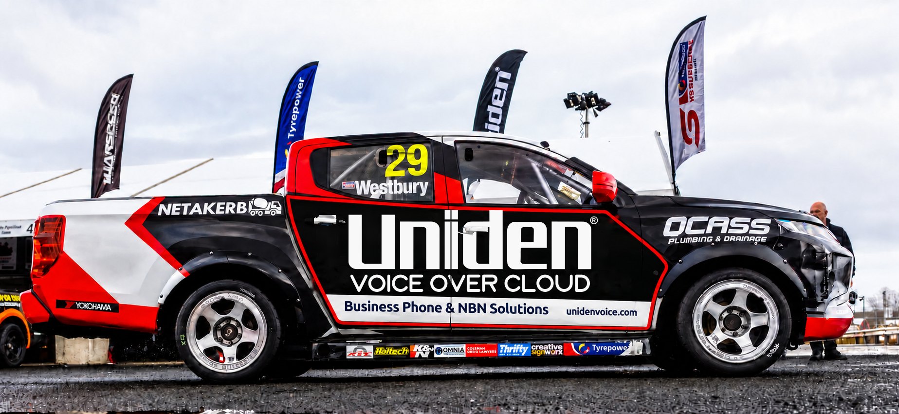 Side view of Jack Westbury's #29 V8 SuperUte in the pits, black with red and white stripes and Uniden Voice Over Cloud branding on the doors
