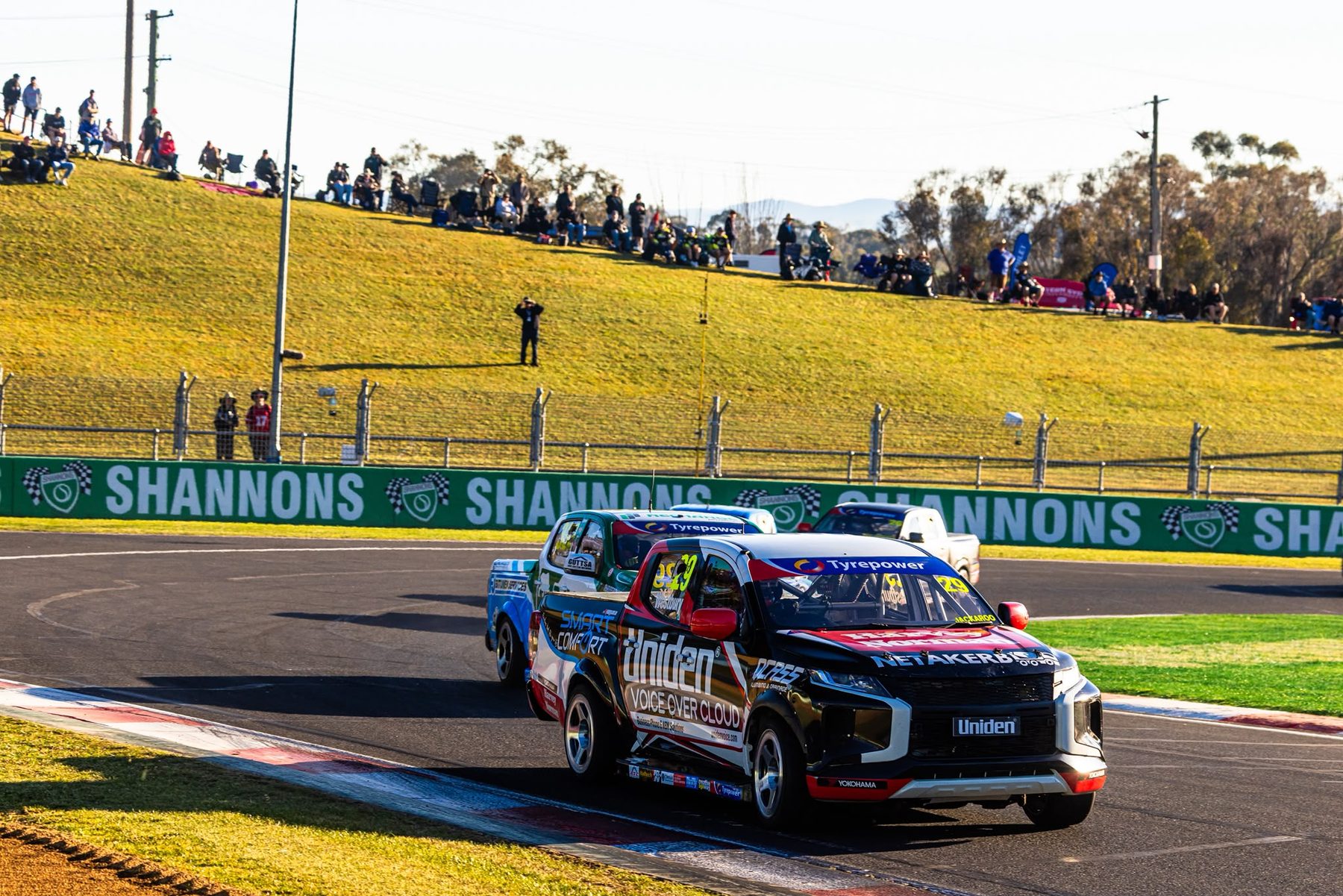 Jack Westbury's #29 Uniden Voice Over Cloud Mitsubishi Triton leading a group of V8 SuperUtes at Mount Panorama, with fans on the hill behind