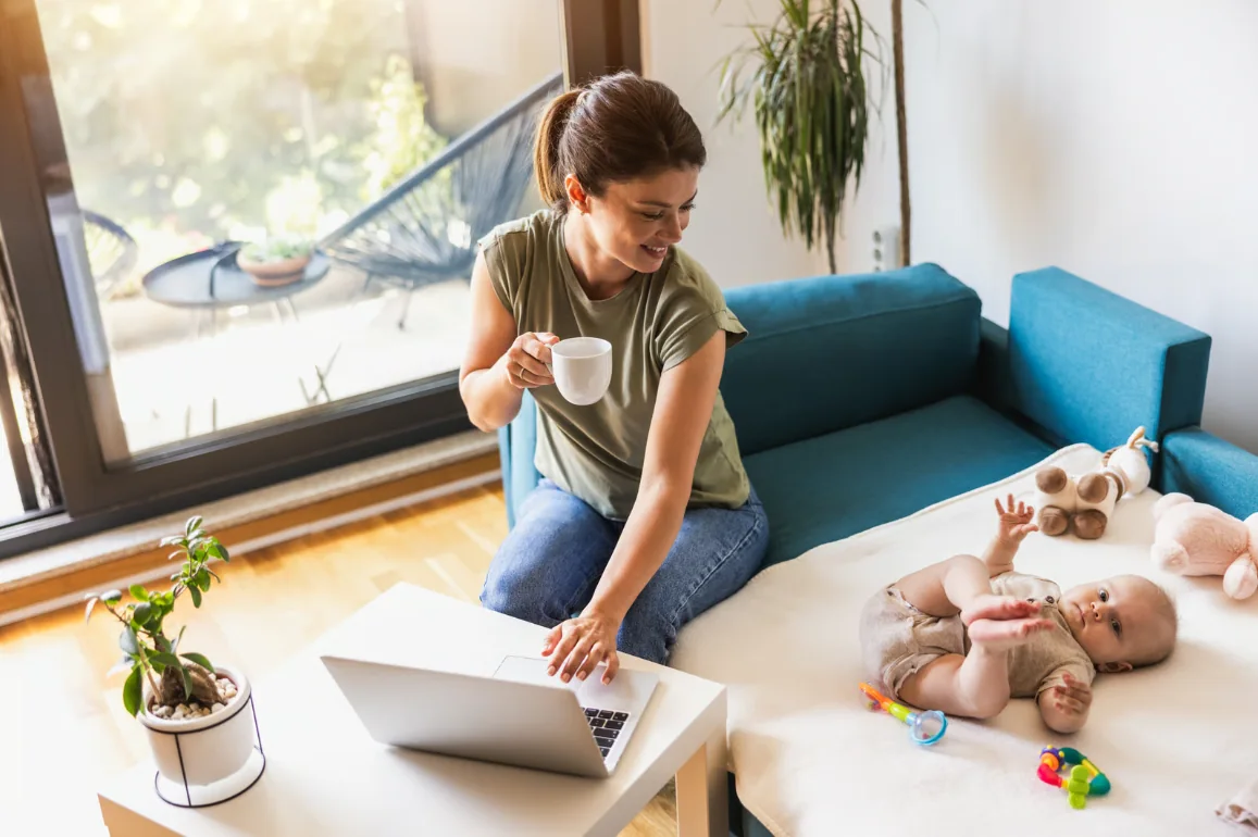 A sole trader working from the lounge on a laptop while keeping an eye on the baby