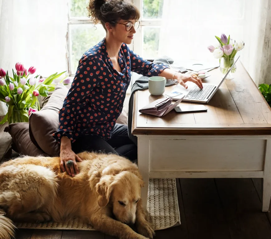 A sole trader working from home at the kitchen table with a laptop and the dog at her feet
